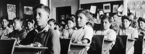 A group of children sitting at desks in a residential school classroom.