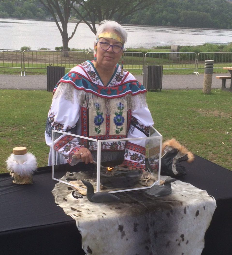 Une femme en tenue autochtone assise à une table au bord d’une rivière à Ottawa, près du Musée canadien de l’histoire.