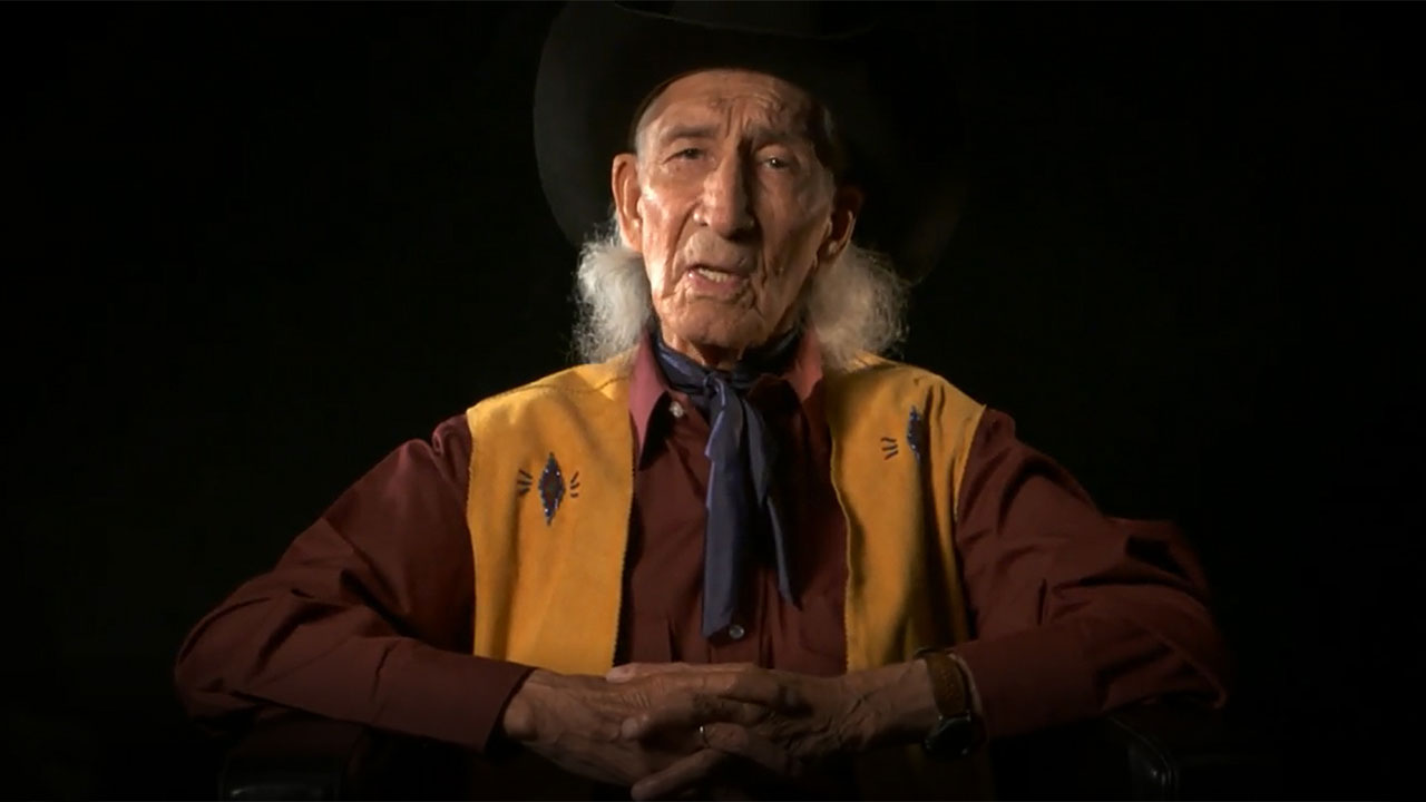 Un homme portant un chapeau de cowboy est assis devant un fond noir au Précipice à Bisons Head-Smashed-In.