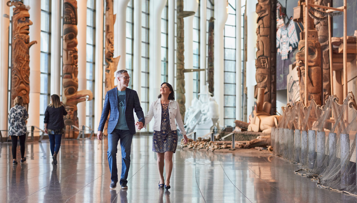 Un couple se promène dans le Musée canadien de l'histoire à Ottawa, admirant de grandes sculptures en bois.