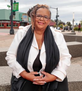 A woman wearing glasses and a scarf is sitting on a bench.