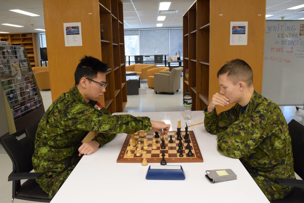 Two cadets in uniform play a game of chess in a library.