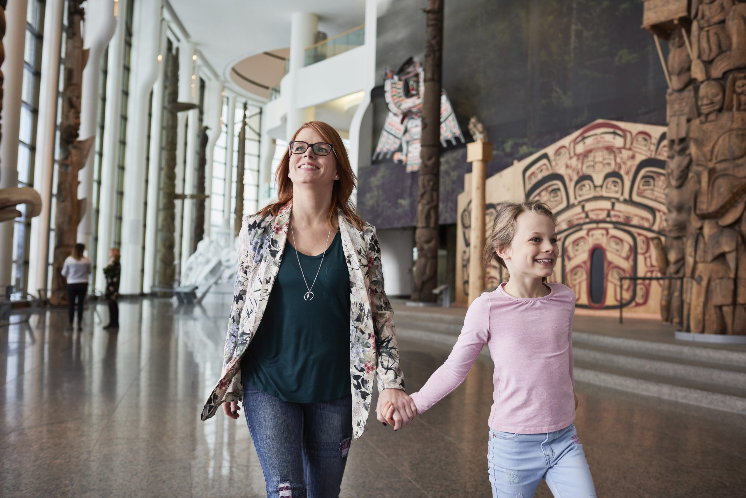 A woman and a child walk hand in hand through a museum, surrounded by various artworks and exhibits on display.